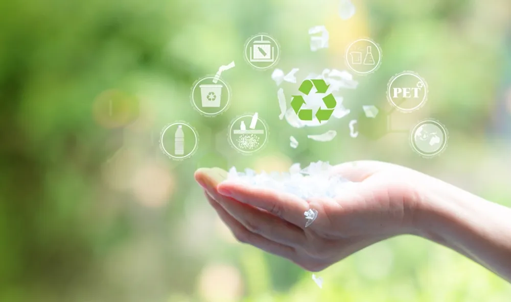 A hand holding recycled plastic flakes beneath a recycling symbol